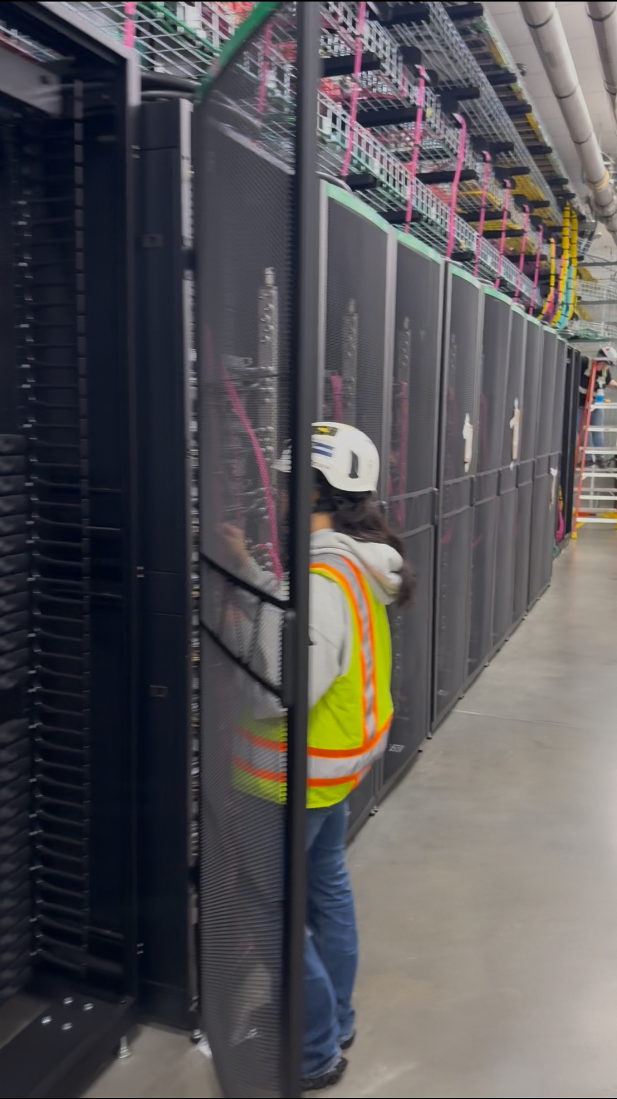 Field worker beside equipment cabinets beneath overhead cable trays.